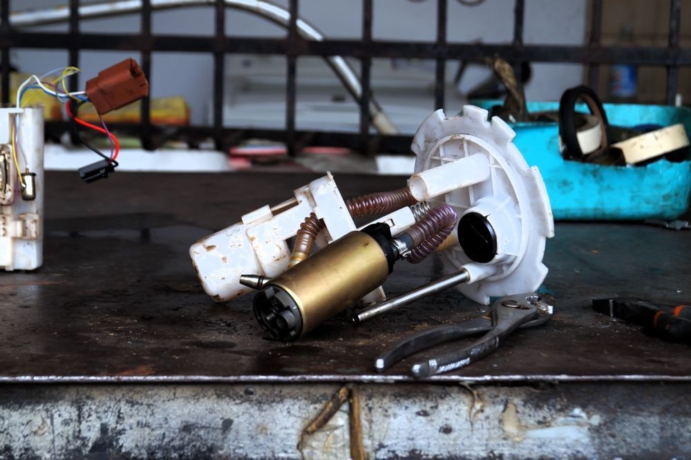 Damaged fuel pump assembly on a workbench with wires and metal parts scattered around