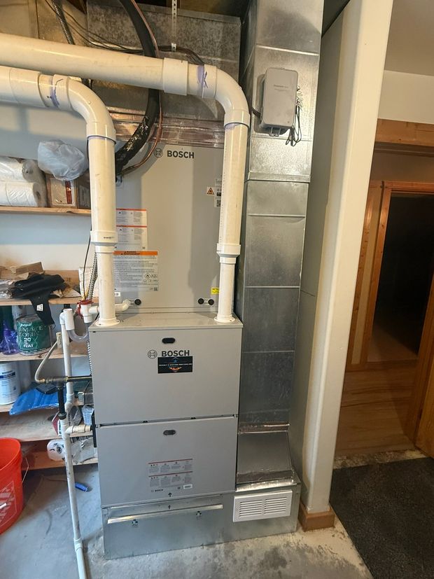 Basement furnace with white ductwork and insulated metal venting beside a doorway