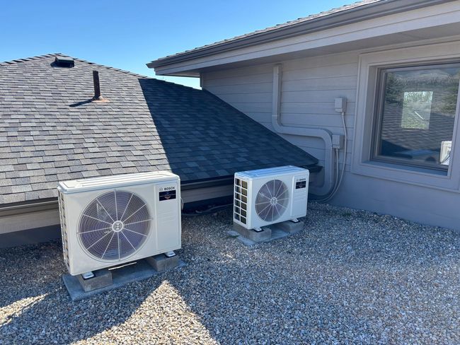 Two outdoor air-conditioning units on a gravel roof beside a house window