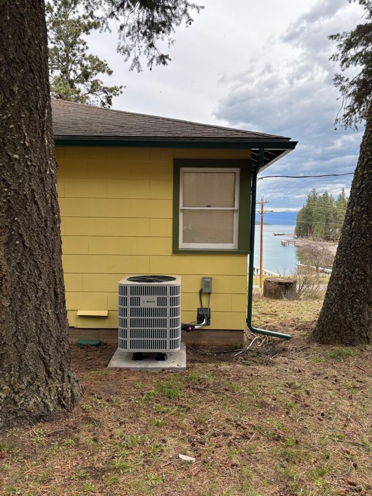 Yellow cabin with an AC unit between two trees, overlooking a lake on a cloudy day