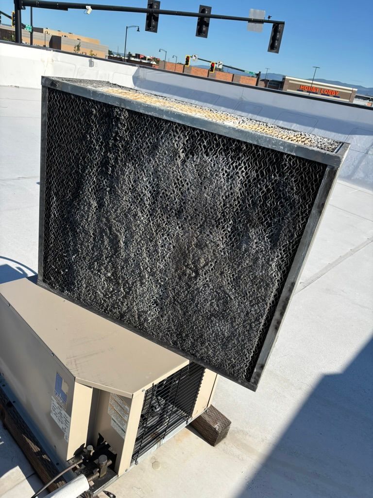 Large black rectangular rooftop unit beside a beige vent on a sunlit roof.