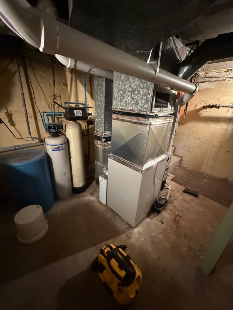 Basement furnace room with metal HVAC ducting, water heater, and utility equipment on concrete floor.