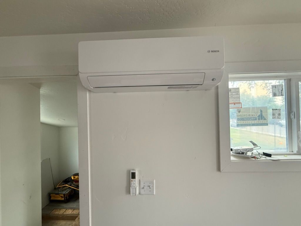 White wall with a mounted air conditioner, small control panel, and a window on the right.