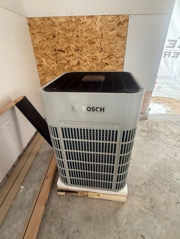 Bosch air conditioner in a corner beside plywood and wall panels on a concrete floor