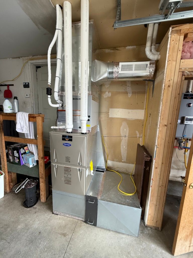 Basement utility room with furnace, white ductwork, shelves, and exposed framing.