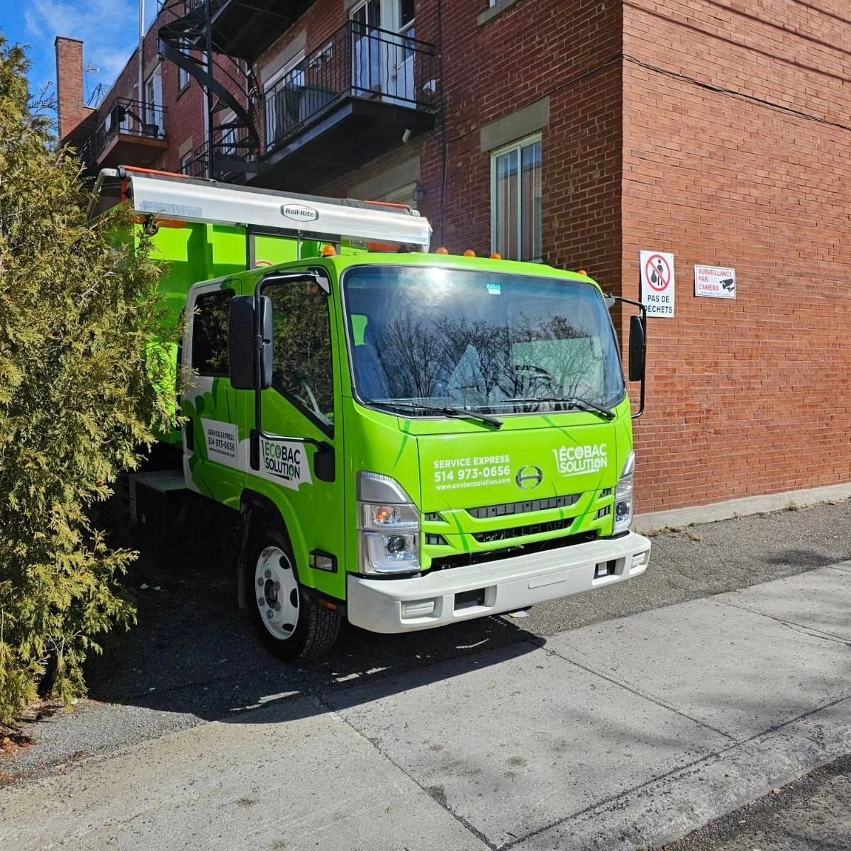 Un camion Eco Bac Solution vert est garé devant un bâtiment en briques.