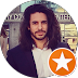 Une personne aux longs cheveux noirs et à la barbe, portant une chemise blanche et un blazer foncé, surmontée d'une icône d'étoile orange.