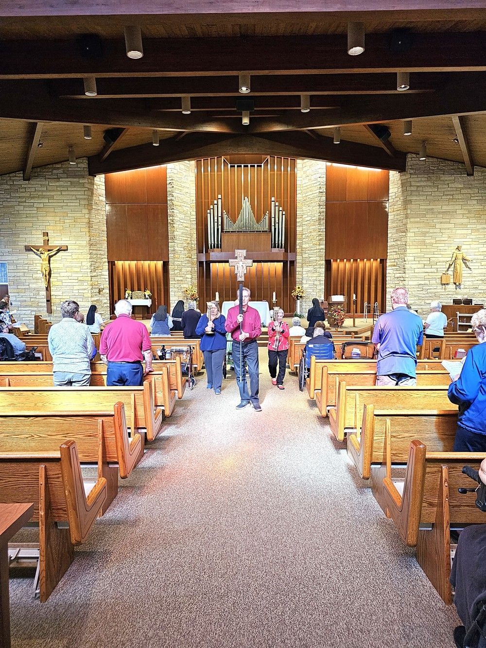 Interior of a church with people standing in the aisles during a service, facing a wood-paneled altar with a pipe organ.