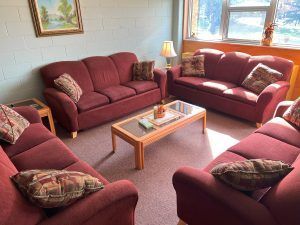 A furnished living room with three red sofas arranged around a rectangular wooden coffee table with a glass top.