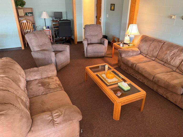 A cozy living room with two brown sofas, a recliner, and a coffee table on a brown carpet.