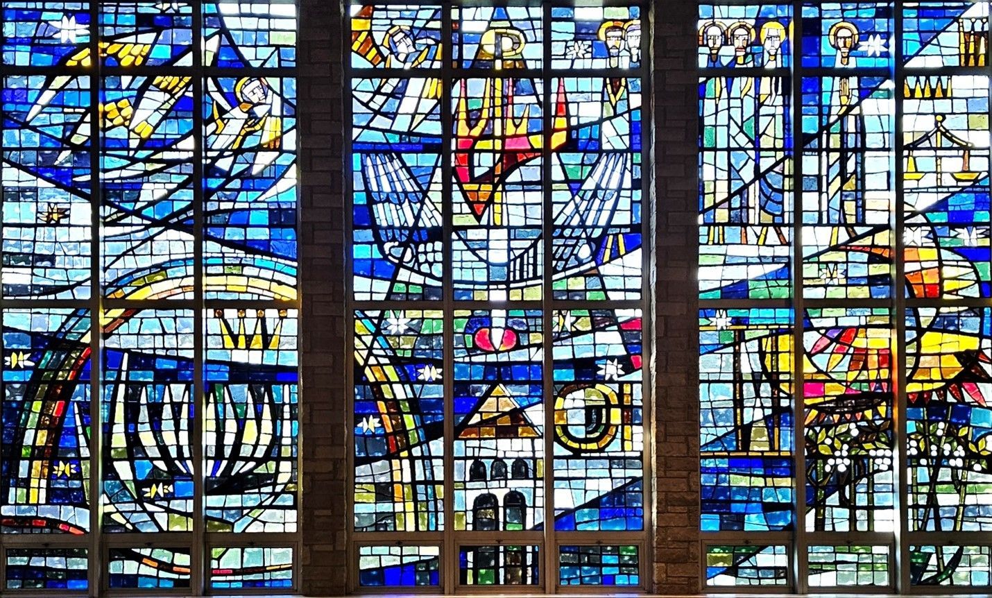 Stained glass window with geometric blue, white, and yellow panels featuring religious and symbolic imagery.