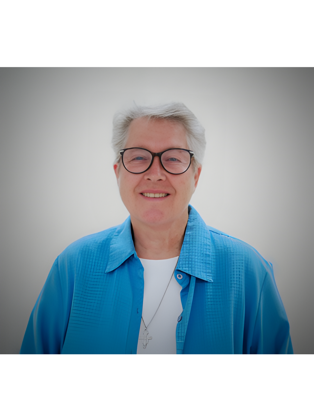 A smiling person wearing glasses, a white shirt, and a bright blue collared overshirt against a plain grey background.