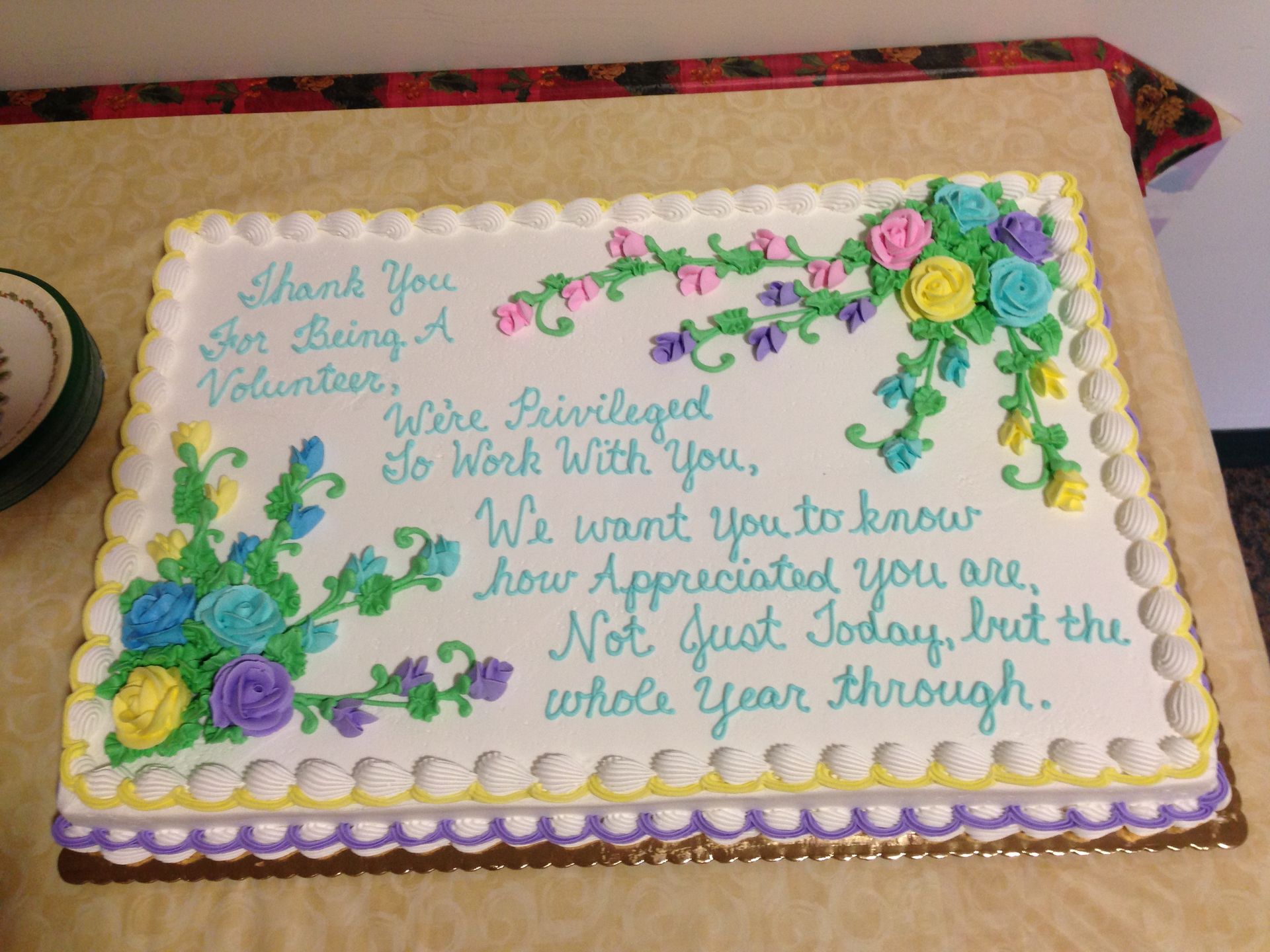 A white sheet cake decorated with colorful floral icing and a message of appreciation for volunteers.