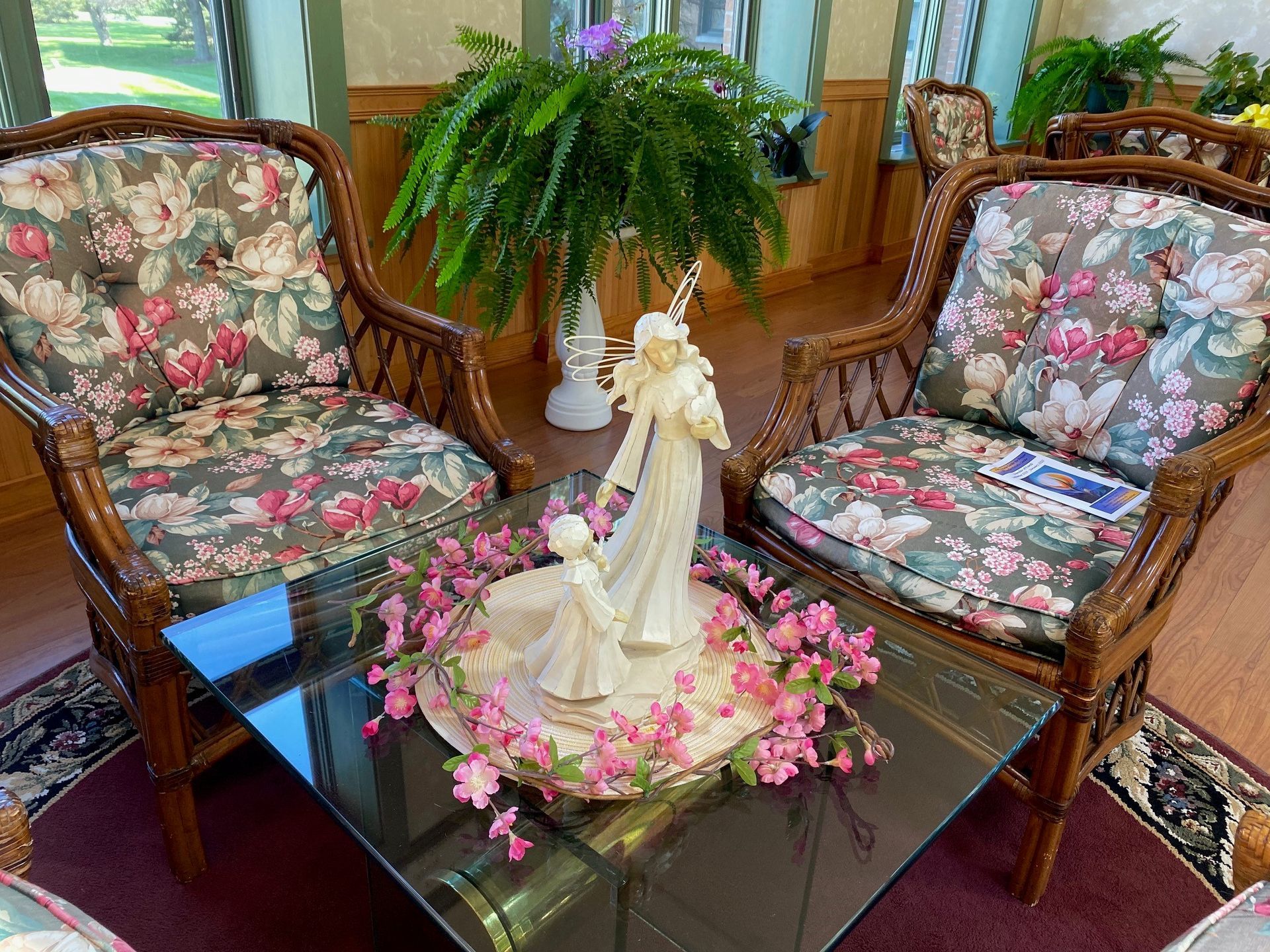 Two floral armchairs with a glass coffee table featuring a central porcelain sculpture surrounded by pink flowers.
