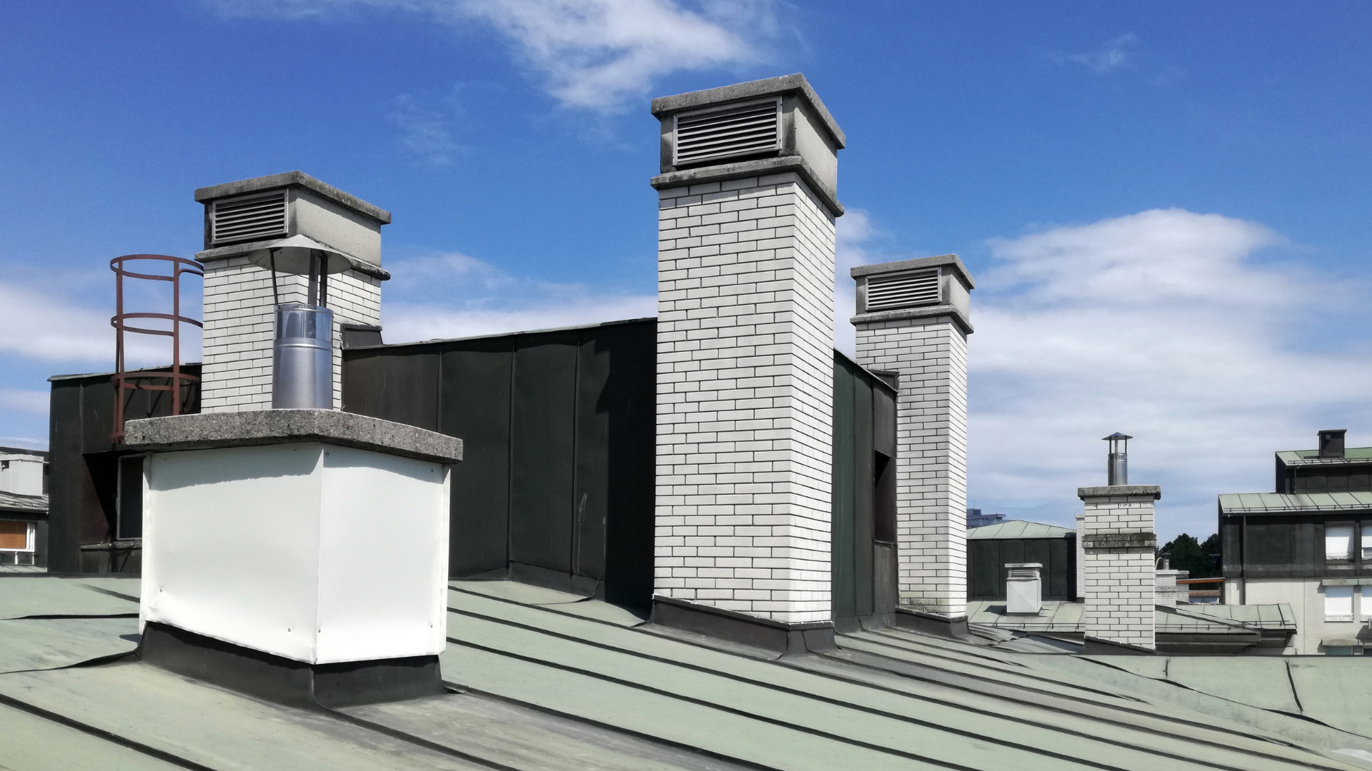 Rooftop with multiple white chimneys and vents under a blue sky.