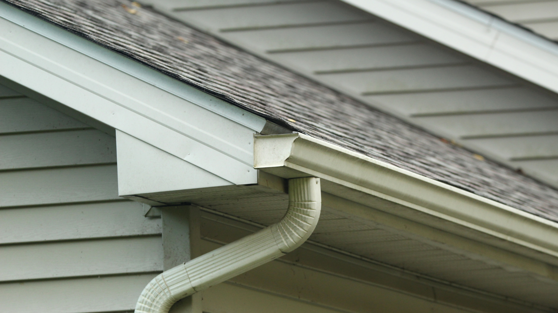 White gutter downspout attached to the corner of a light gray house roof.