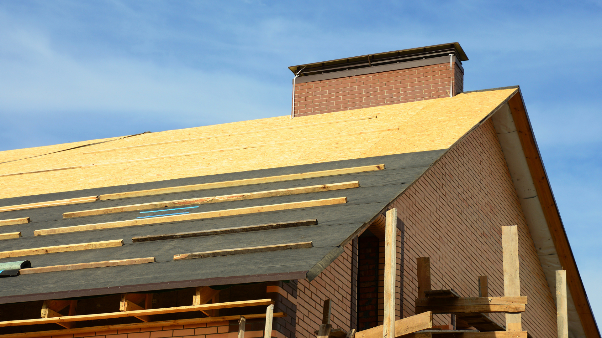 Partially roofed house with brick chimney and yellow insulation under a blue sky