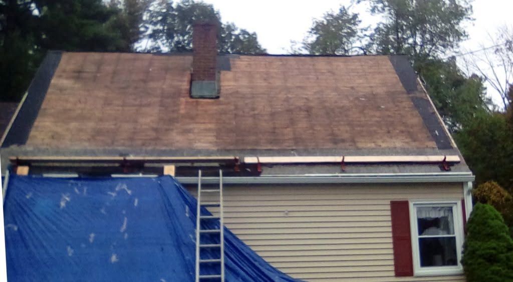House roof under repair with blue tarp and ladder against beige siding