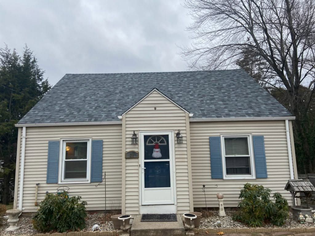 Small beige house with blue shutters and a blue front door under a cloudy sky