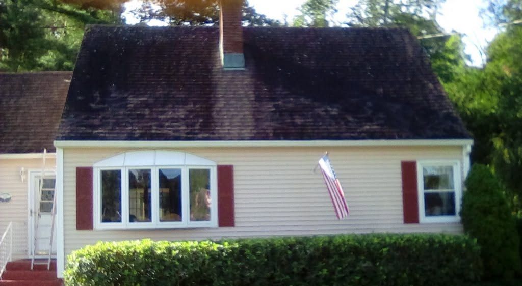 White house with dark roof, red shutters, and an American flag hanging beside the front windows.