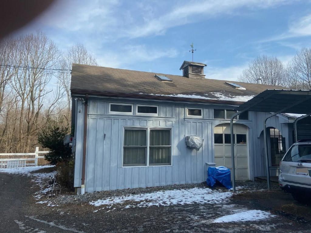 Snow-dusted blue house exterior with broken roof and parked car beside it