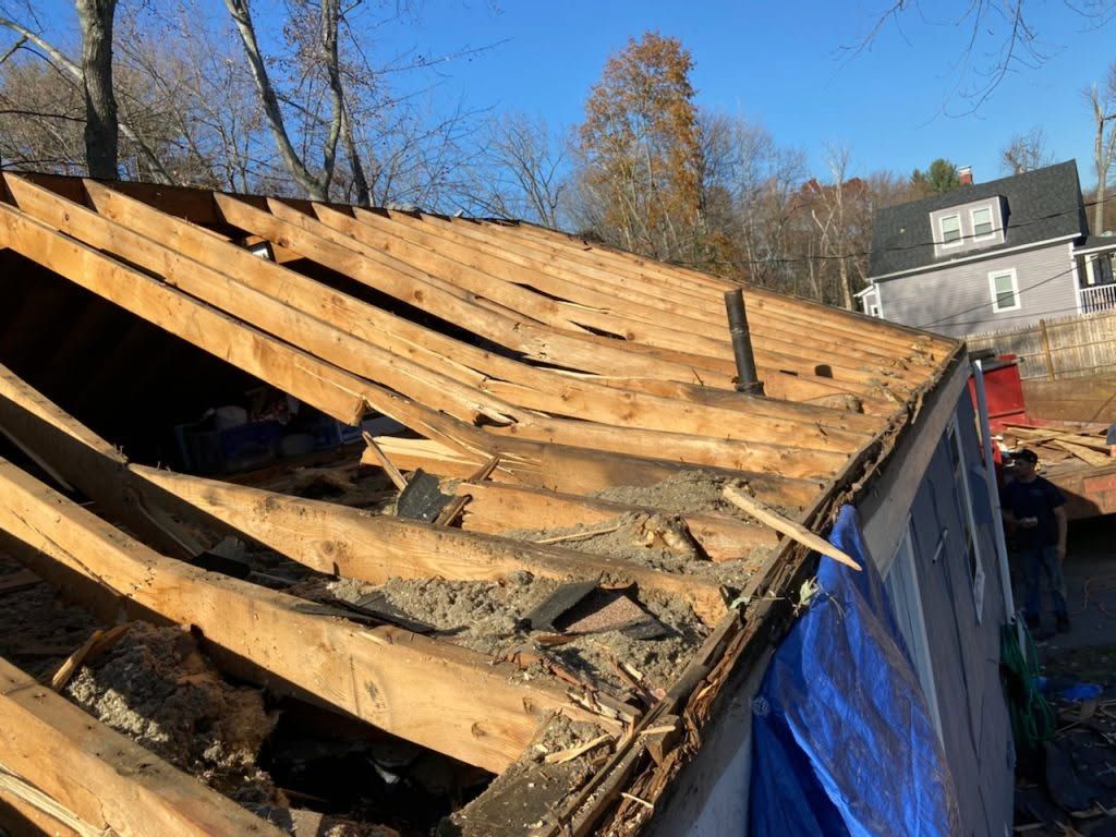 Partially collapsed roof with exposed wooden rafters and blue tarp on a house