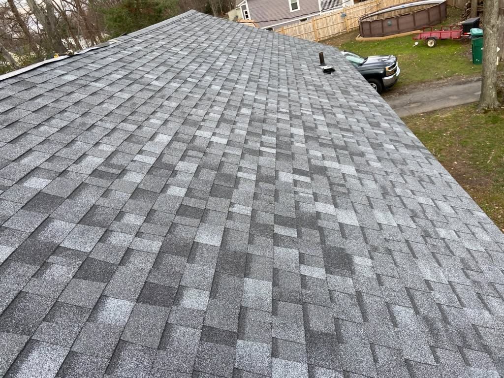 Gray shingled roof on a house, viewed from above with a yard and parked car in the background