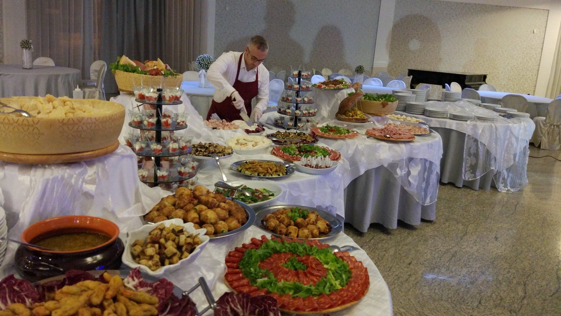 Tavolo a buffet con piatti assortiti e un cameriere che sistema il cibo in una sala per banchetti.
