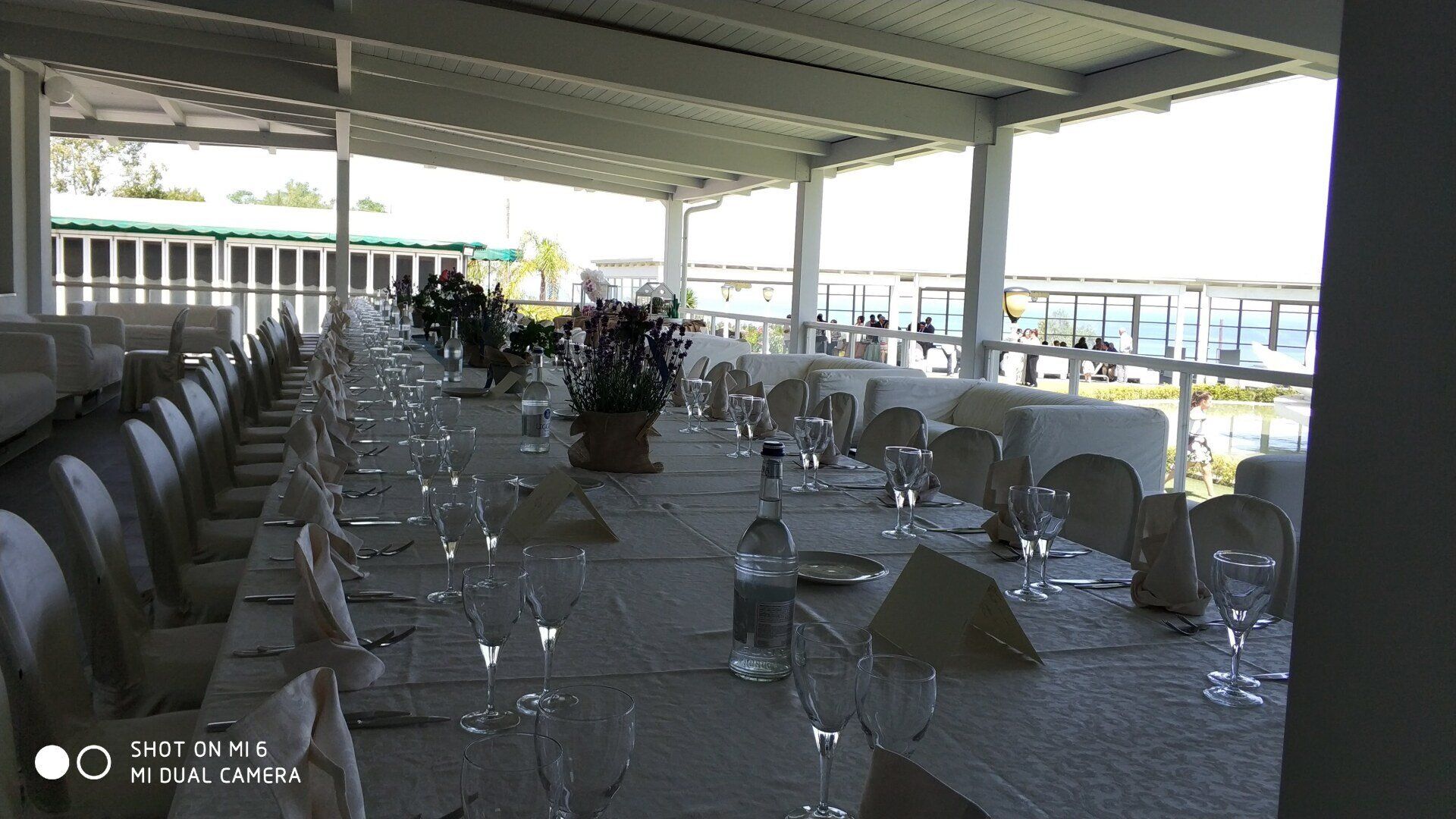 Apparecchiate i tavoli da pranzo con tovaglie bianche e bicchieri sotto una terrazza esterna coperta con vista sull'acqua.