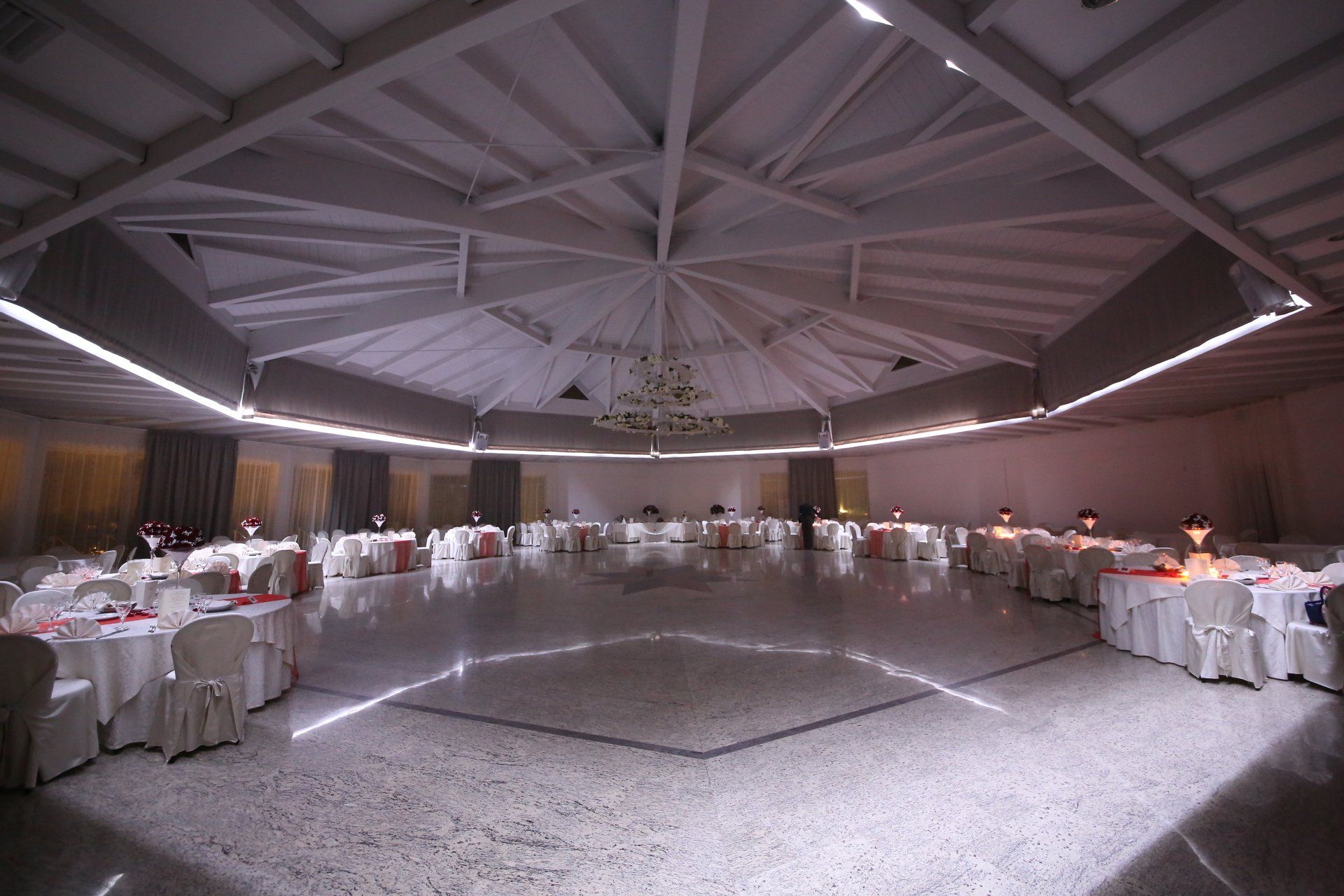 Sala per banchetti con tavoli rotondi ricoperti da tovaglie bianche sotto un grande soffitto circolare.