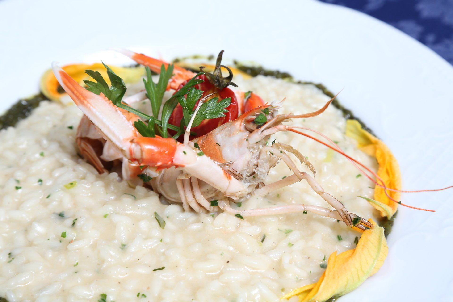 Risotto ai frutti di mare con gamberi, erbe aromatiche e petali di fiori edibili, servito su un piatto bianco.