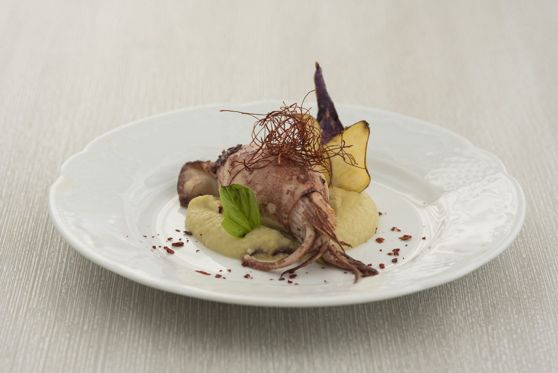Un piatto bianco con sopra un calamaro e del purè di patate su un tavolo.