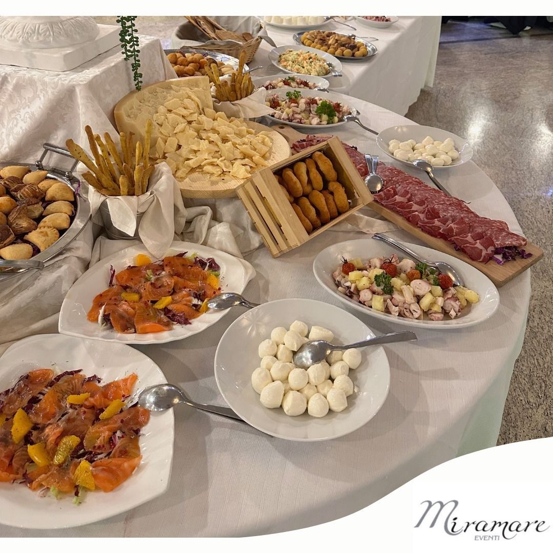 Tavolo da buffet con assortimento di antipasti, pasticcini e dessert su vassoi bianchi.