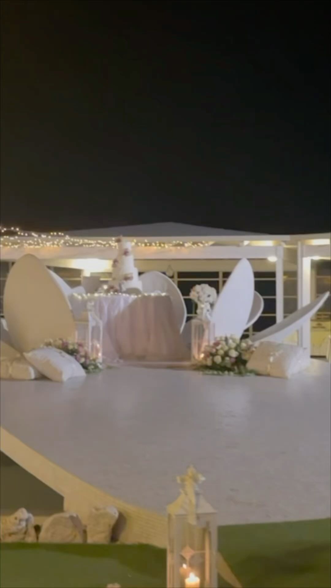Palco per eventi all'aperto decorato con composizioni floreali bianche e fondale drappeggiato di notte