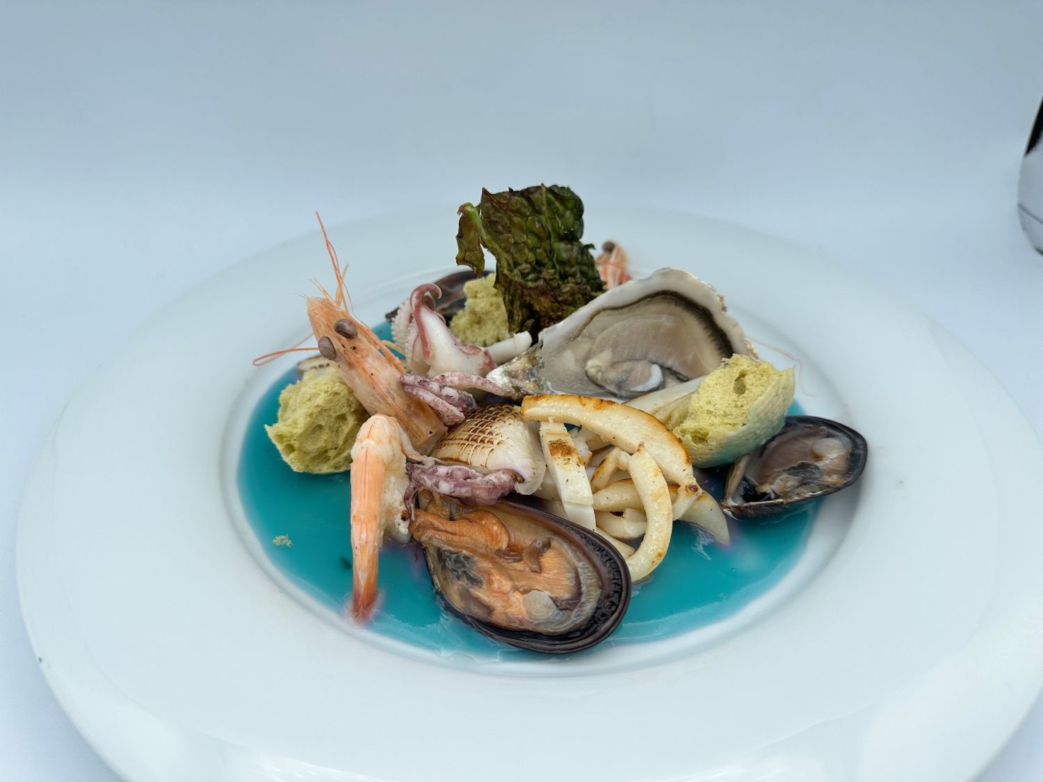 Un piatto bianco condito con frutti di mare e salsa blu