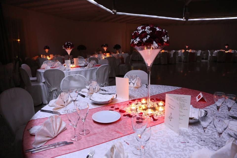 Tavolo da banchetto con centrotavola floreale rosa e decorazioni a lume di candela in una sala eventi scarsamente illuminata.