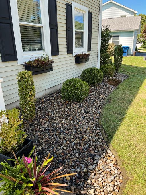Exterior of a beige house with black shutters, flower boxes, and a rock-covered garden bed.