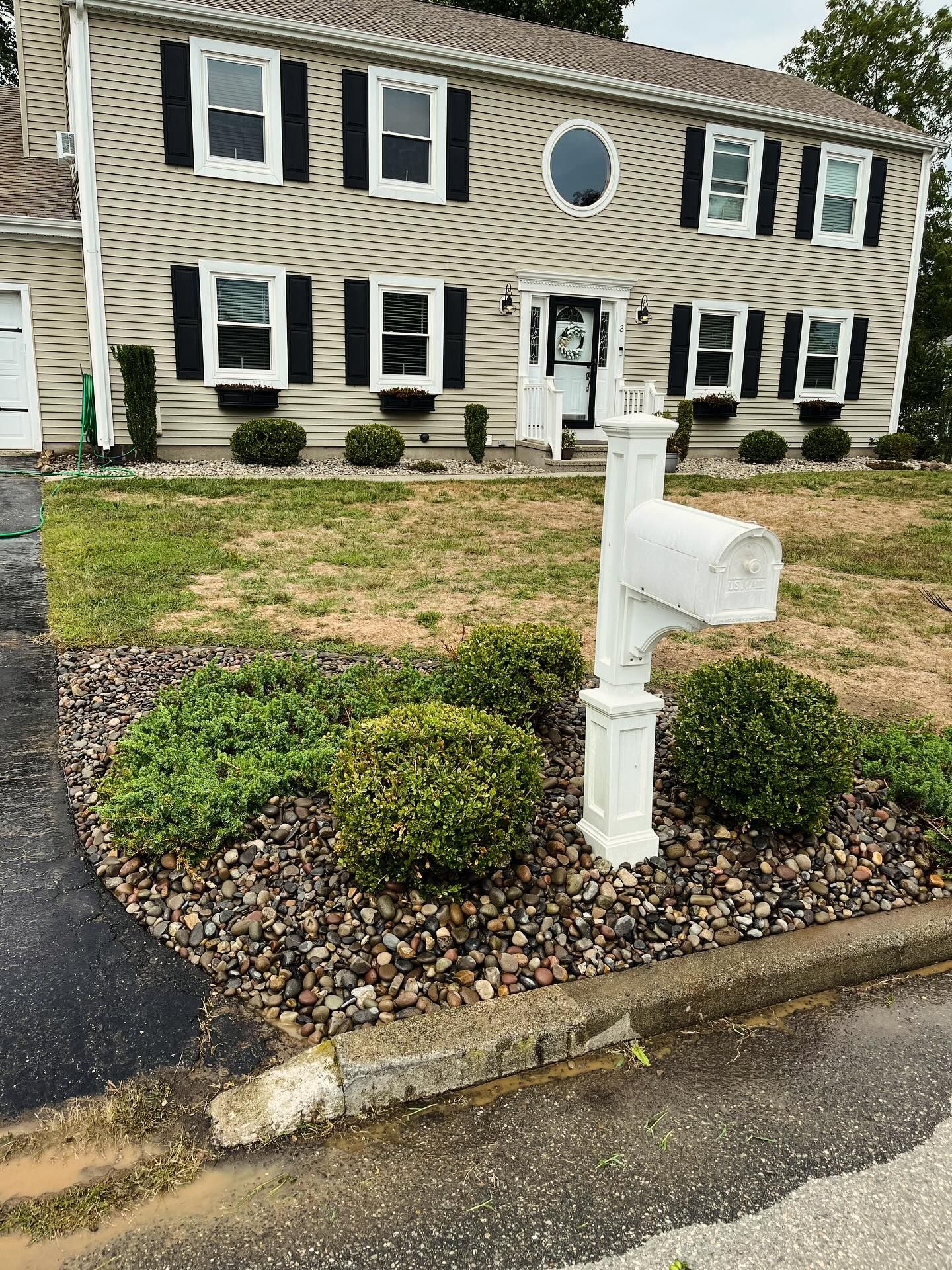 Trench dug in a grassy yard, leading to a house with black siding, and an electrical box.