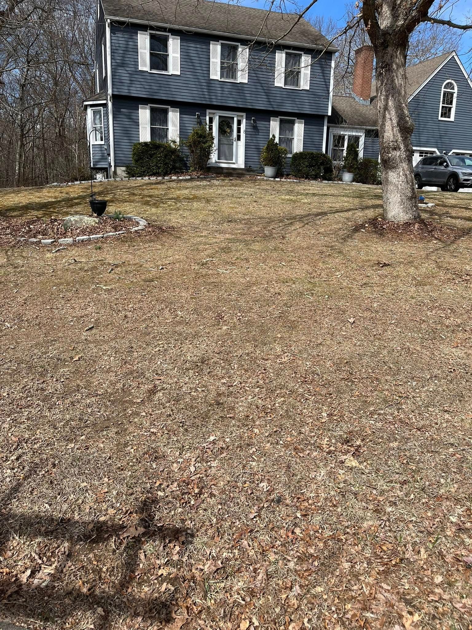 Blue house with white trim, front yard covered in brown leaves, sunny day.