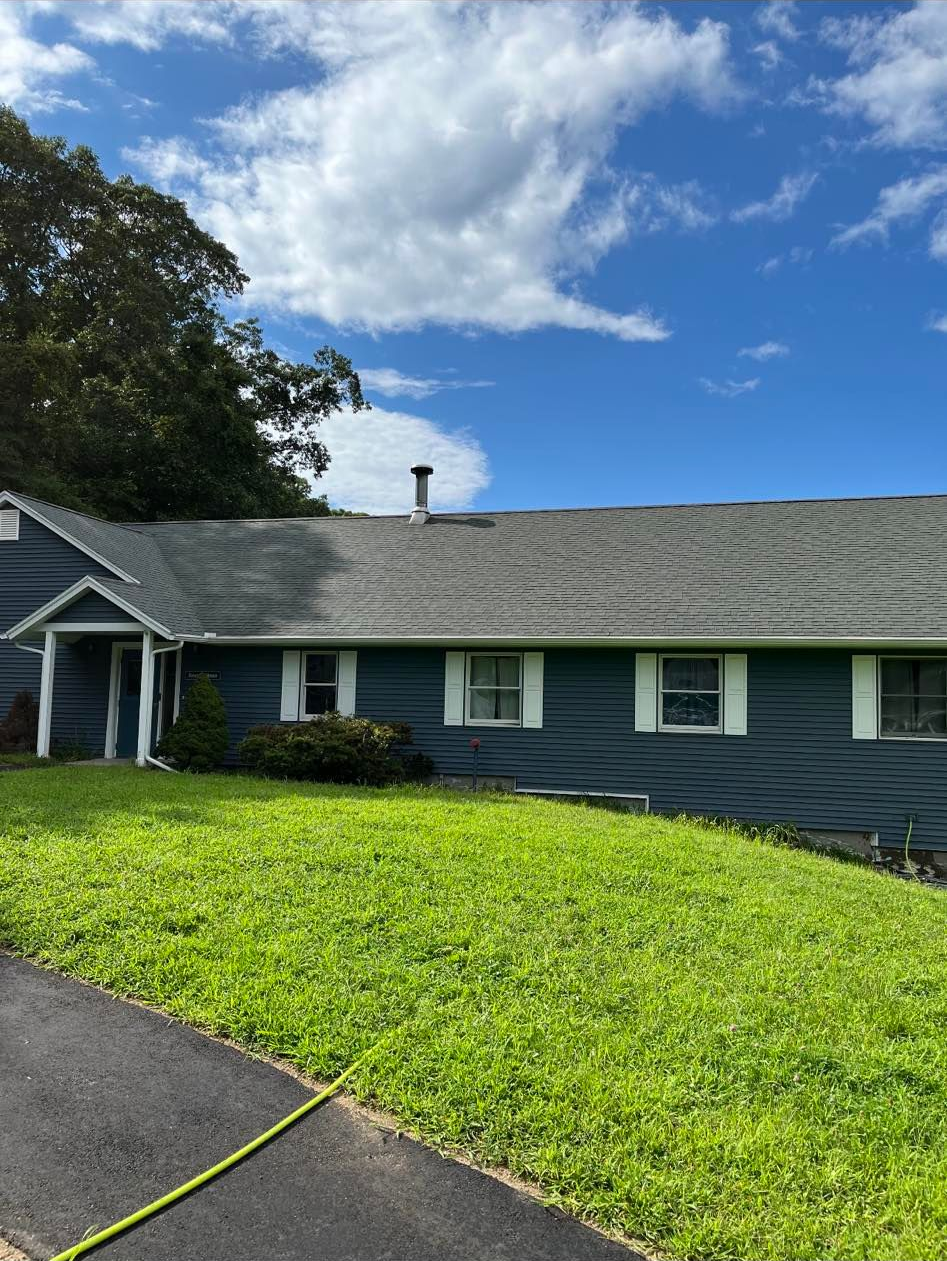Blue house with gray roof, green lawn, and blue sky with clouds.
