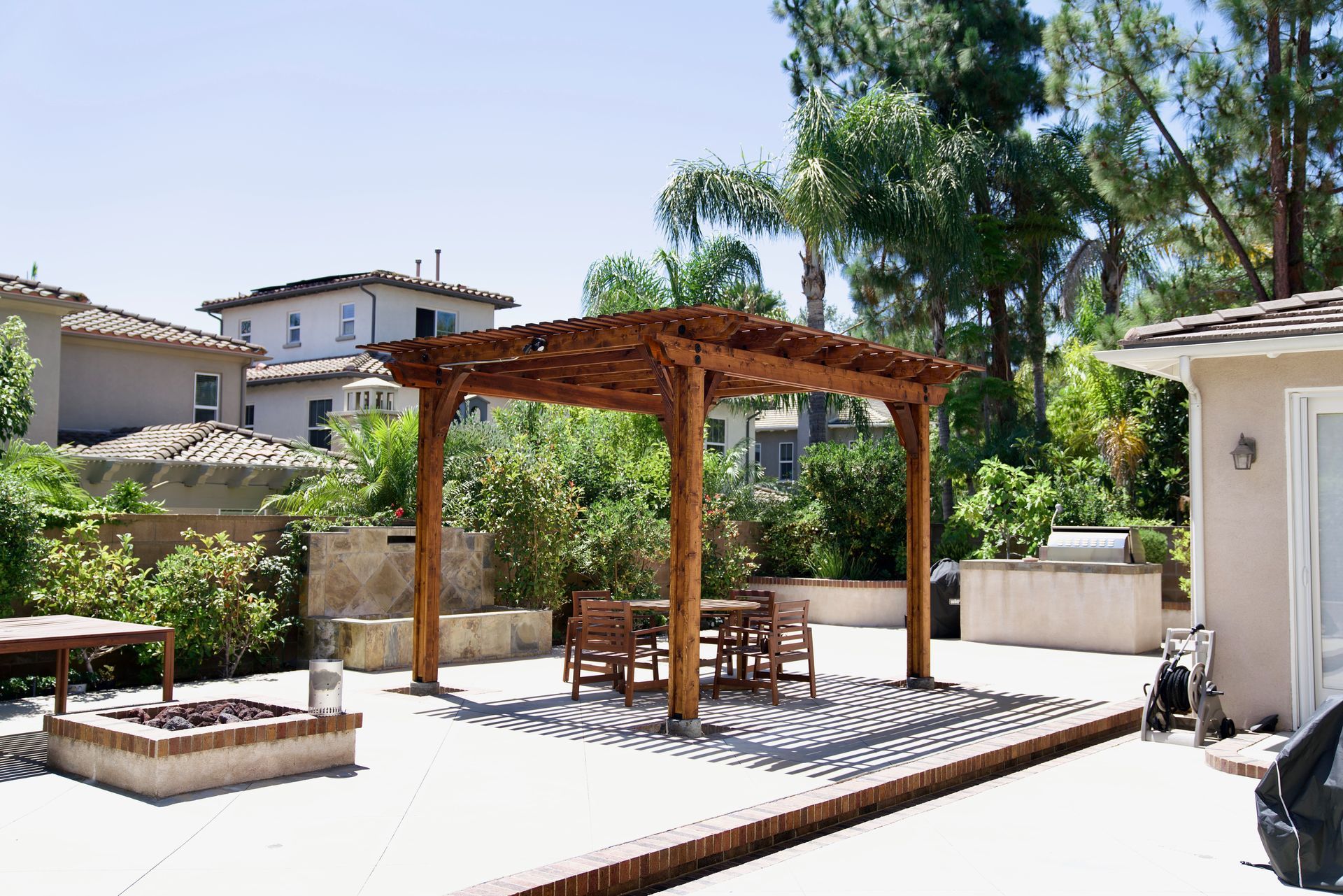 Backyard patio with wooden pergola, dining table, and potted plants under a clear blue sky
