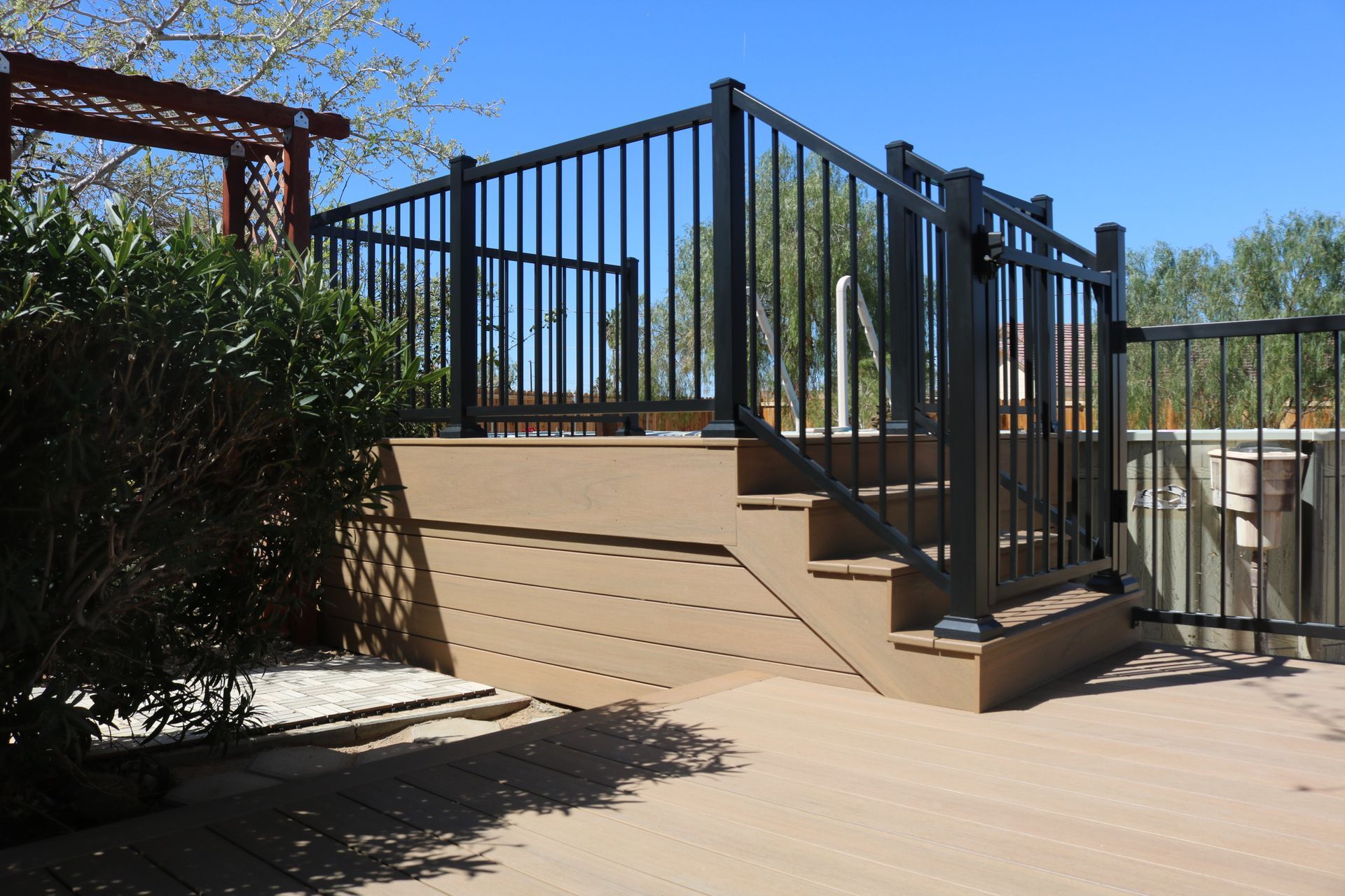 Black metal railing and stairs beside a tan deck in a sunny backyard
