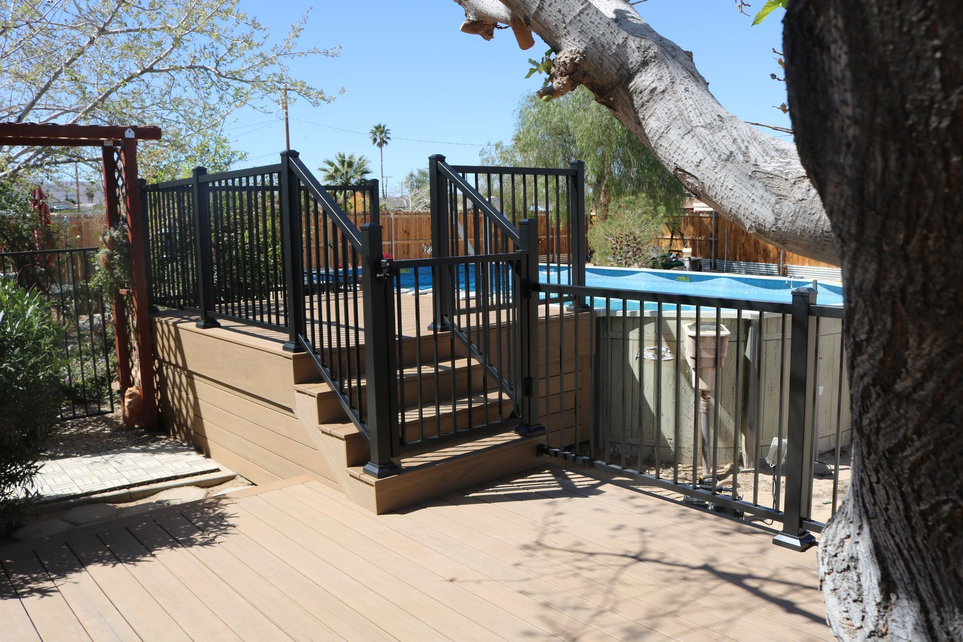 Black fenced pool deck with steps, blue pool water, and a tree in the foreground