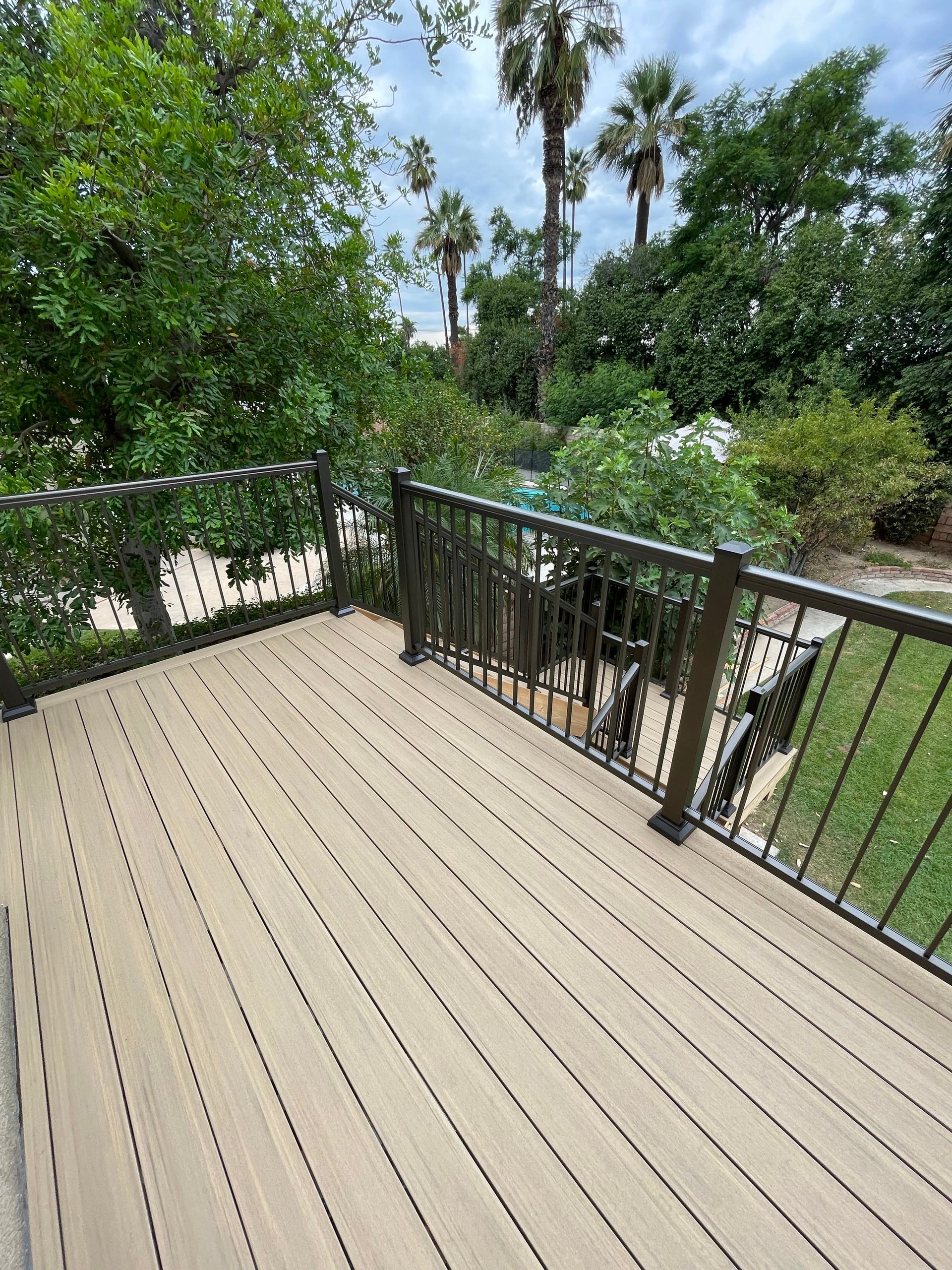 Wooden deck with black railing overlooking a lush green backyard and trees