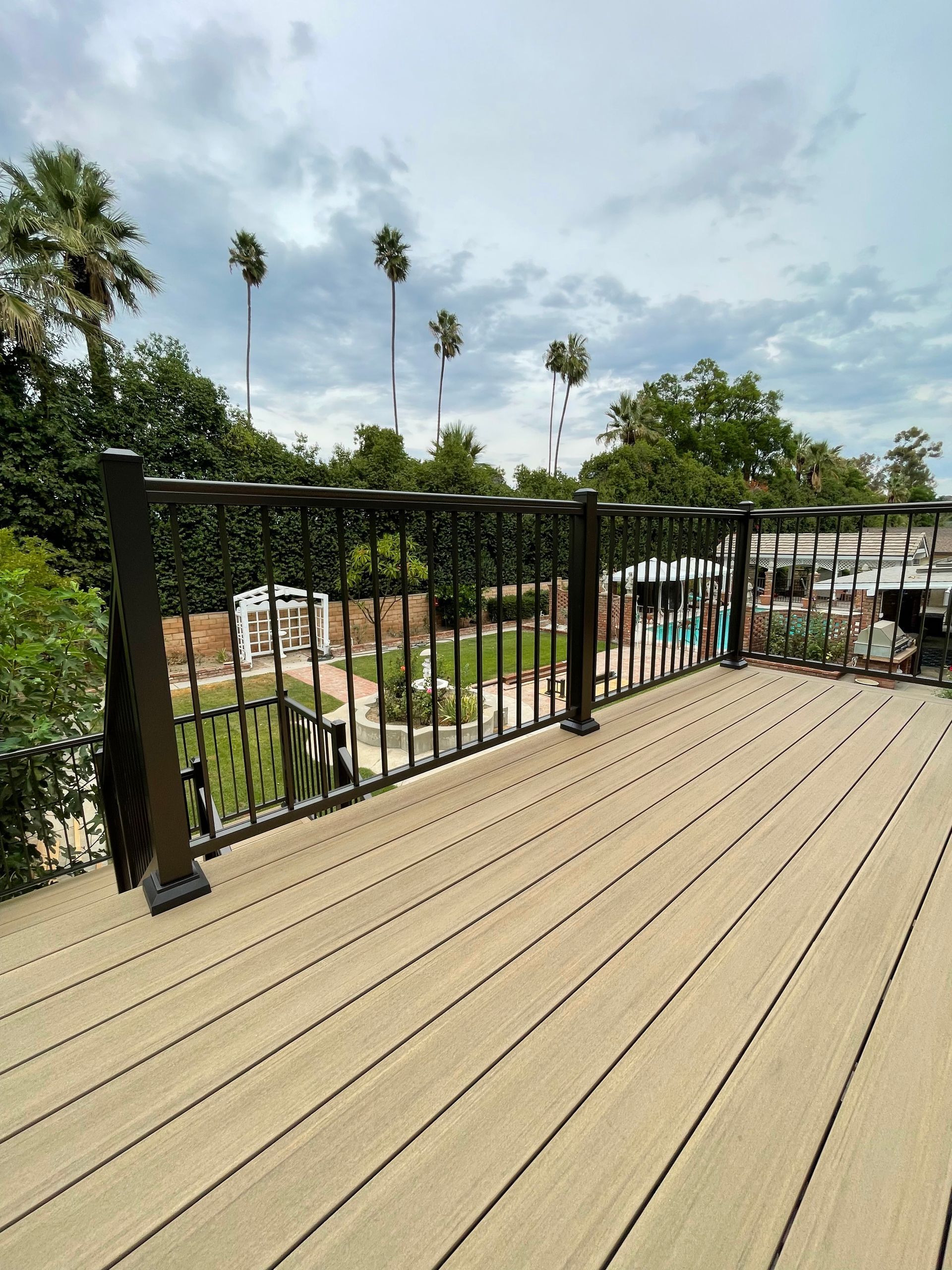 Wooden deck with black railing overlooking a tropical resort and palm trees under a cloudy sky