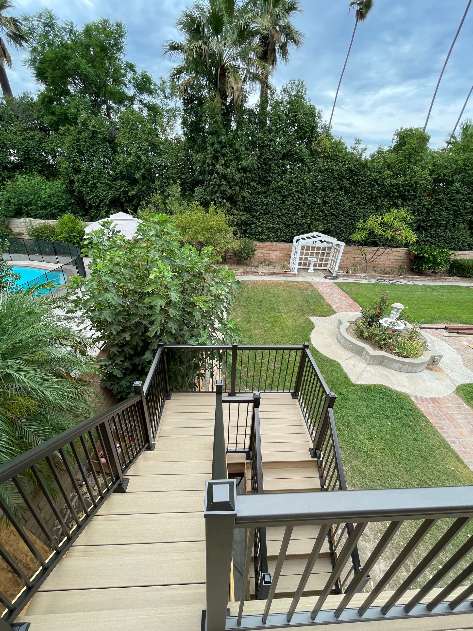 Wooden stairway descending to a garden path with white bench, trees, and a glimpse of a pool