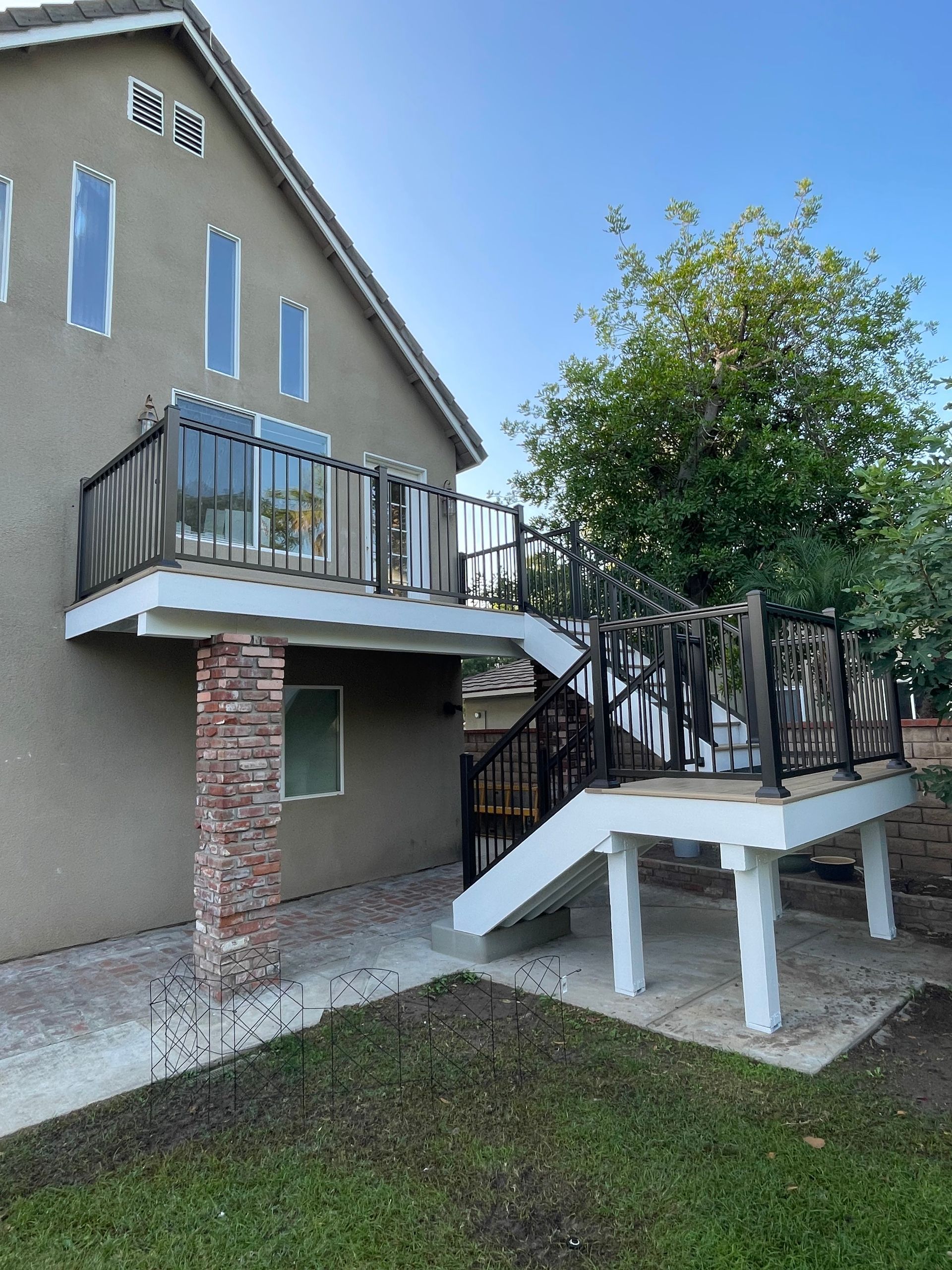Exterior staircase and balcony on a beige house with black railings and brick support columns.