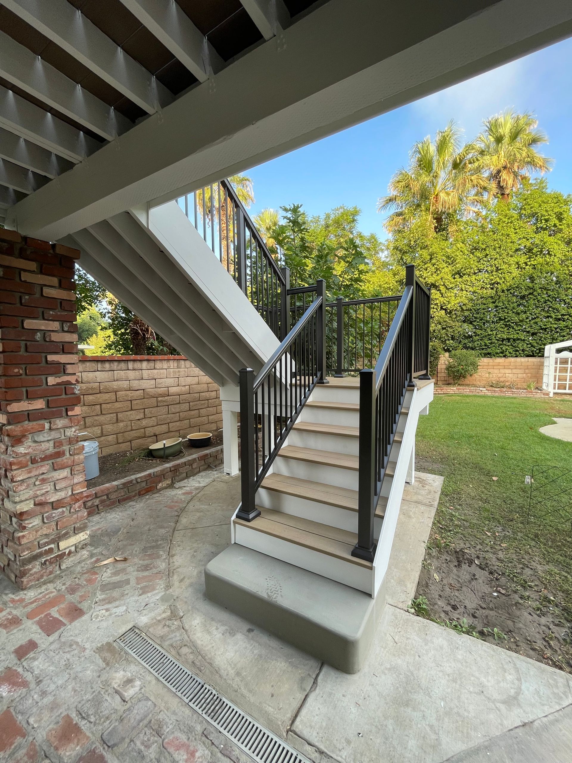 Outdoor staircase with black railings leading to an upper deck beside a brick house and lawn