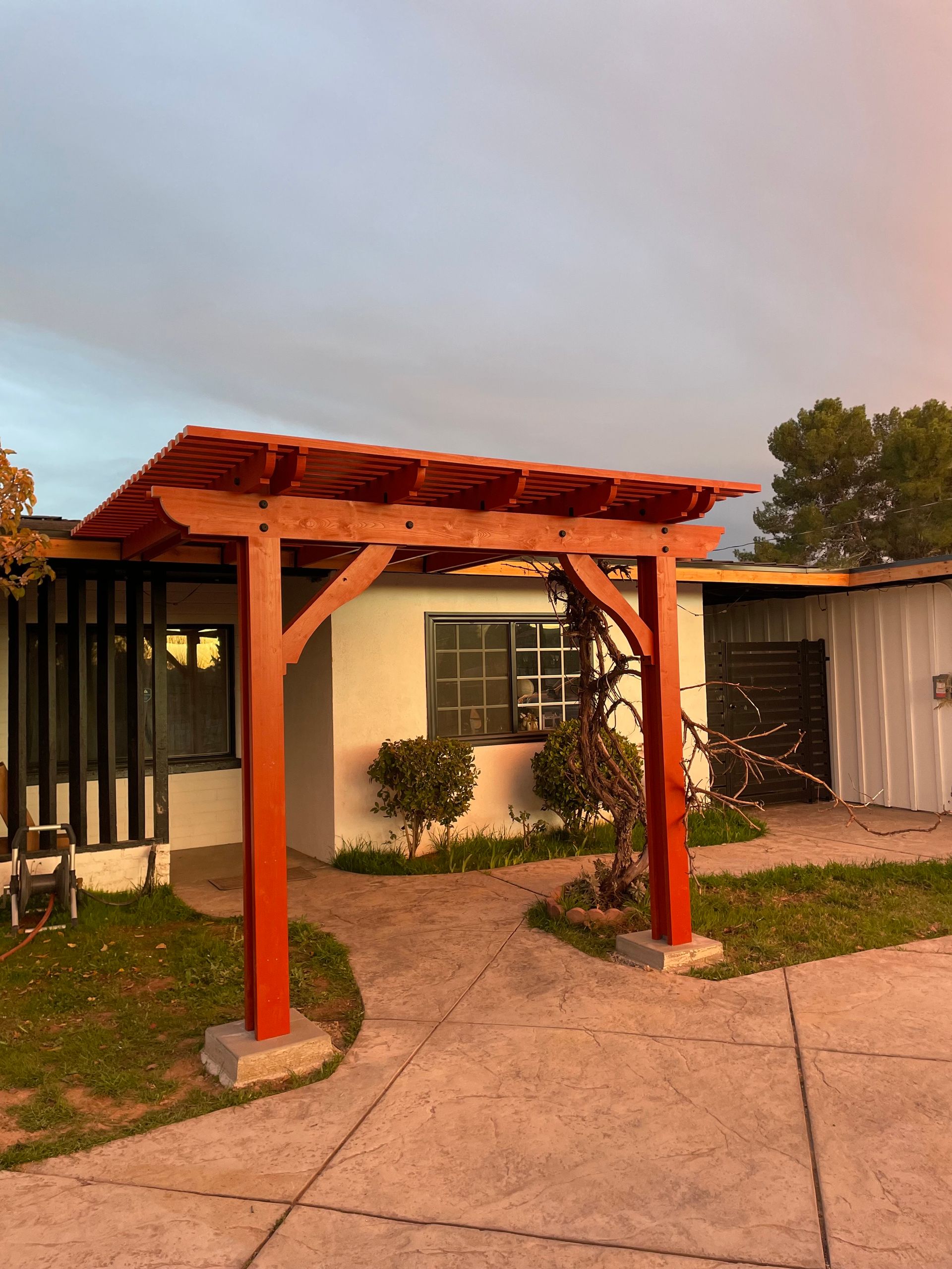 Red wooden pergola over a small courtyard beside a building at dusk
