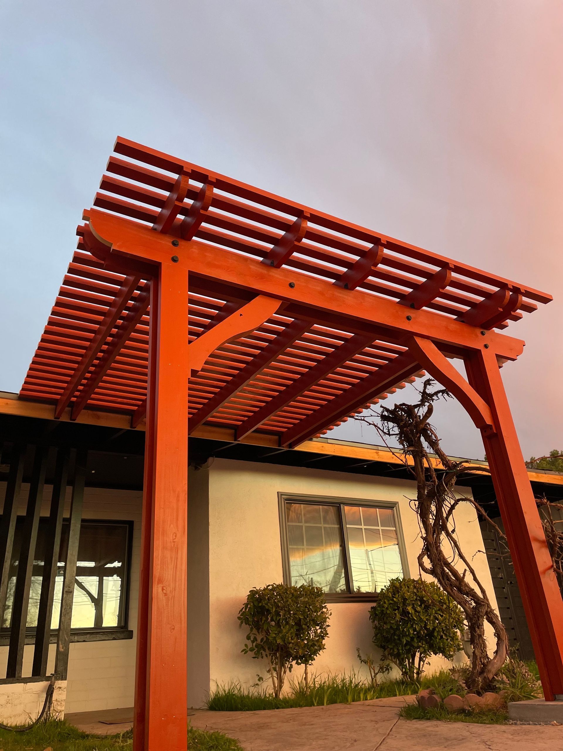 Wooden pergola over a patio beside a house at sunset